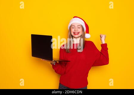 Giovane donna nel cappello di santa tiene il laptop nelle sue mani e lavora su uno sfondo giallo Foto Stock