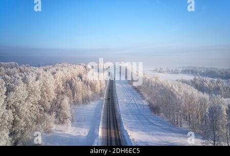 Siberian strada rurale asfaltata sotto la neve. Paesaggio rurale invernale siberiano con alberi di betulla ricoperti di brina. Scatto aereo Foto Stock