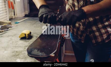 Manutenzione sci. Rimozione della cera in eccesso dal raschietto in plastica della base da sci. Servizio sci e riparazione. Lavoratore negozio invernale che fa base r Foto Stock