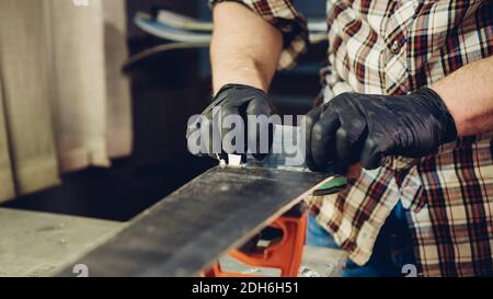 Manutenzione sci. Rimozione della cera in eccesso dal raschietto in plastica della base da sci. Servizio sci e riparazione. Lavoratore negozio invernale che fa base r Foto Stock