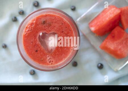 Una vista dall'alto del frullato di cocomero in un bicchiere con un cubo di ghiaccio a forma di cuore Foto Stock