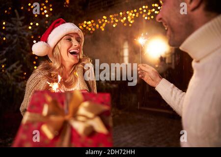 Felice dolce coppia sorridente in abiti caldi con sparklers dentro le mani trascorrono molto tempo vicino a casa Foto Stock