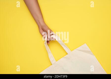 La mano femmina tiene una borsa di tessuto beige vuota vicino alle maniglie su uno sfondo giallo, rifiuto di pla Foto Stock