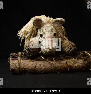 Un giocattolo a cavallo amigurumi uncinetto con una pila decorativa di legno su sfondo nero Foto Stock