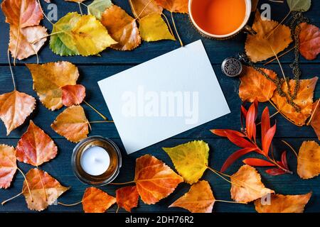 Un biglietto d'auguri vuoto o invito con una tazza di tè, foglie d'autunno e una candela, un mockup autunnale di cancelleria, overhead piatto Foto Stock