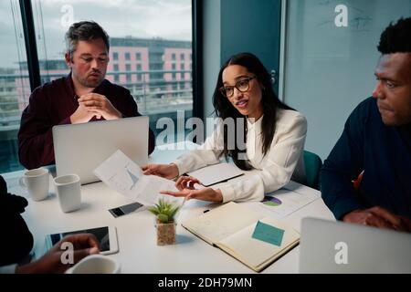 Giovane donna d'affari afro-americana intelligente che le mostra un grafico colleghi di sesso maschile multietnici in un ufficio moderno: discussione sul lavoro di squadra tra Foto Stock