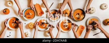 Piatto di mani umane pranzo con zuppa di crema di zucca in piatti con panna acida, semi di zucca e crostini su un tavolo bianco semplice decorato con zucche, vista dall'alto. Cibo sano e confortevole Foto Stock