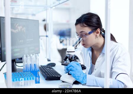 Microbiologo in laboratorio di ricerca che fa esperimenti scientifici guardando attraverso microscop. Camice da laboratorio che indossa una tecnologia moderna durante gli esperimenti scientifici in ambiente sterile. Foto Stock