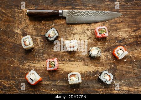 Diversi tipi di sushi con coltello giapponese su sfondo di legno. Vista dall'alto Foto Stock