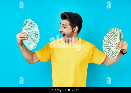 Felice uomo eccitato che tiene banconote di denaro su sfondo blu Foto Stock