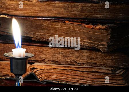 Pila di vecchi libri in pelle-legati indossati e candela bruciante al buio. Messa a fuoco selettiva. Tasto basso Foto Stock