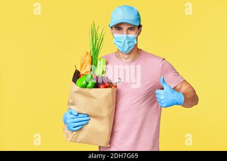 Uomo di consegna che dà cibo in sacchetto di carta indossando maschera facciale E guanti come protezione per COVID-19 Foto Stock