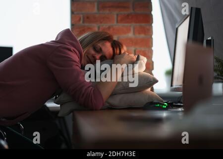 Donna d'affari che dorme sui cuscini al tavolo in ufficio Foto Stock