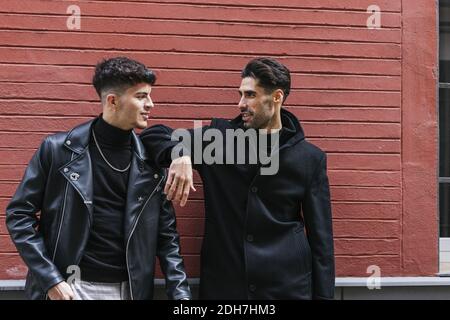 Un primo piano di giovani amici che indossano cappotti neri e. bluse che si trovano di fronte a un muro rosso Foto Stock