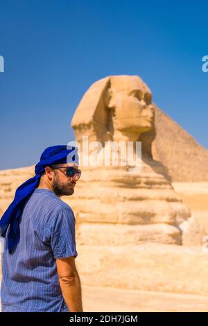 Un giovane turista che si gode e si ammira la Grande Sfinge di Giza vestita di turbano blu e blu, il Cairo, Egitto Foto Stock