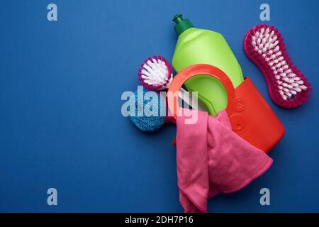 Cestello rosa con spugne di lavaggio, spazzole e detergente in bottiglia di plastica verde su bac blu Foto Stock