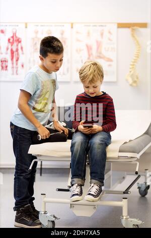 Fratelli che usano smartphone al tavolo esame in clinica ortopedica Foto Stock