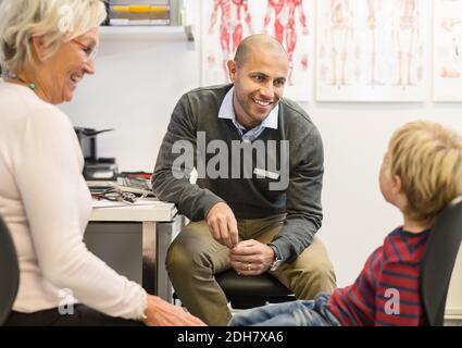 Donna anziana felice che guarda il nipote che parla con il medico a. ambulatorio ortopedico Foto Stock