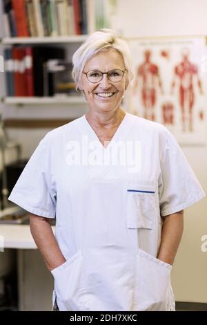 Ritratto di Felice chirurgo ortopedico senior in piedi con le mani in mano tasche in clinica Foto Stock