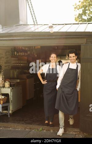 Ritratto a lunghezza intera di proprietari sorridenti che si trovano all'esterno del ristorante Foto Stock