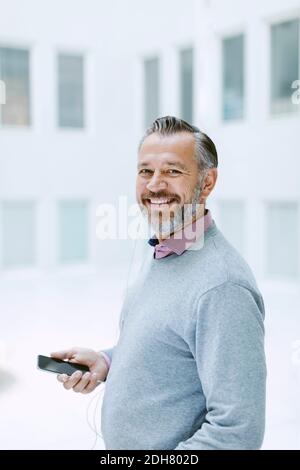 Ritratto di felice uomo d'affari che ascolta musica attraverso smartphone in ufficio Foto Stock