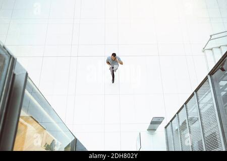 Vista ad alto angolo di un uomo d'affari con il telefono cellulare mentre si cammina in un ufficio moderno Foto Stock