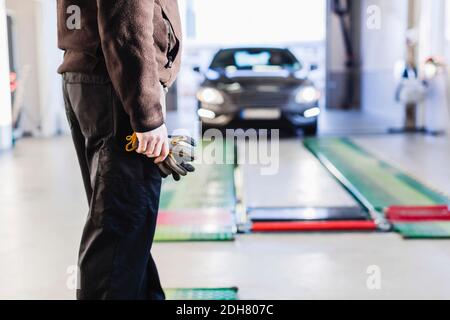 Sezione centrale del meccanico in piedi davanti all'auto che viene verso sollevatore idraulico Foto Stock