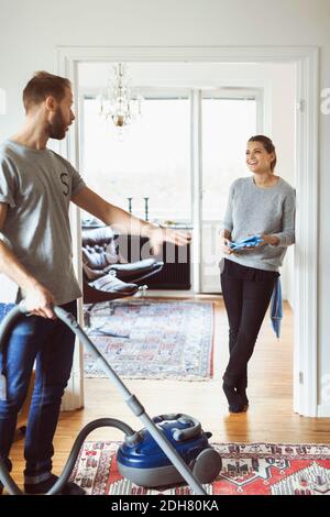 Uomo che usa l'aspirapolvere mentre parla con una donna a casa Foto Stock