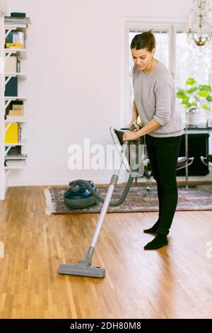 Donna che aspira il pavimento di legno duro a casa Foto Stock