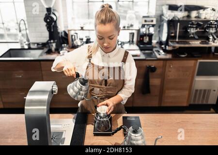 Vista ad angolo alto del barista femminile che versa acqua bollente all'interno filtro caffè al banco caffè Foto Stock