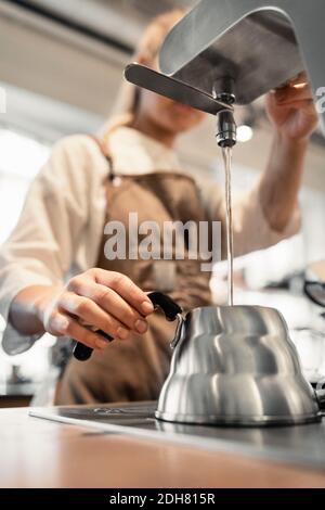 Barista femminile che versa acqua bollente nella caffettiera dalla macchina al banco del caffè Foto Stock