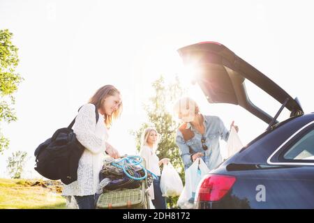 Amici di sesso maschile e femminile che scaricano auto sul campo contro chiaro cielo Foto Stock