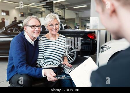 Felice coppia anziana che guarda il venditore nello showroom dell'automobile Foto Stock