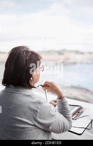 Vista posteriore della donna d'affari anziana che utilizza il dispositivo vivavoce tramite il finestrino in ufficio Foto Stock