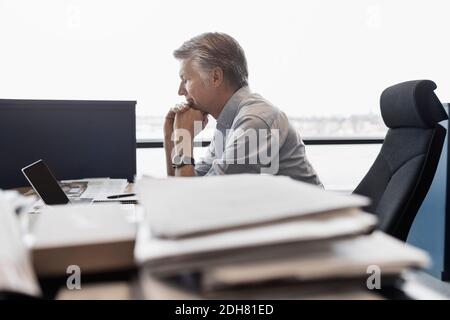 Vista laterale di un uomo d'affari con un computer portatile alla scrivania in ufficio Foto Stock