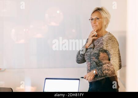 Donna d'affari anziana premurosa che guarda via in ufficio Foto Stock