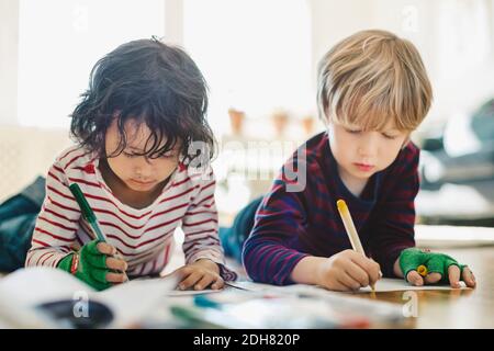 Amici che si stendano sul pavimento mentre si colorano in libri a casa Foto Stock