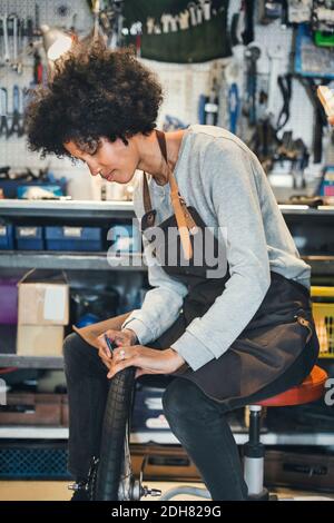 Mid adult femmina meccanico che ripara il pneumatico della bicicletta in officina Foto Stock