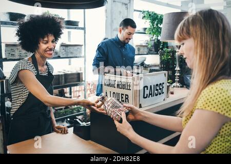 Lavoratore felice che dà vaso di vetro al cliente in negozio Foto Stock