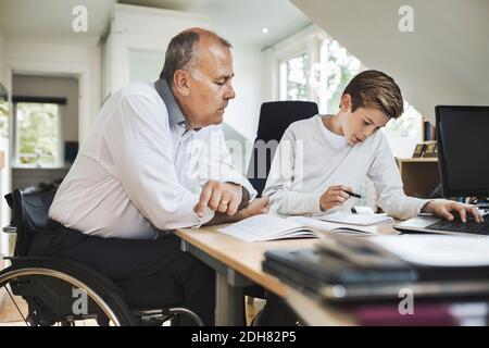 Il padre disabile assiste il figlio nel fare i compiti a casa Foto Stock