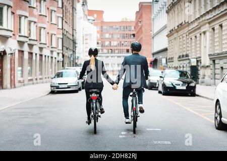 Vista posteriore del personale d'affari che tiene le mani mentre si guida in bicicletta sulla strada Foto Stock