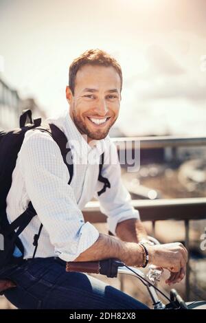 Ritratto di felice uomo d'affari appoggiato in bicicletta contro il cielo Foto Stock