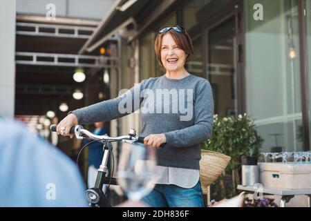 Donna anziana felice che guarda via mentre tiene la bicicletta all'aperto Foto Stock