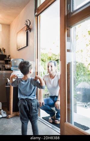 Donna felice che guarda il figlio mentre accovacciava sulla porta Foto Stock