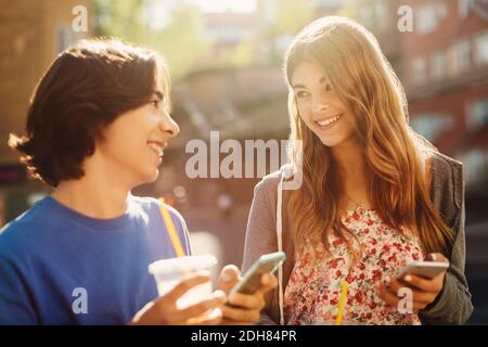 Felici adolescenti che si guardano l'un l'altro mentre si tengono in possesso di smartphone all'aperto Foto Stock