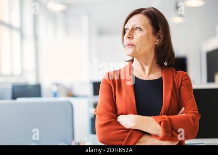 Donna d'affari in piedi braccia incrociate mentre si guarda via in ufficio Foto Stock
