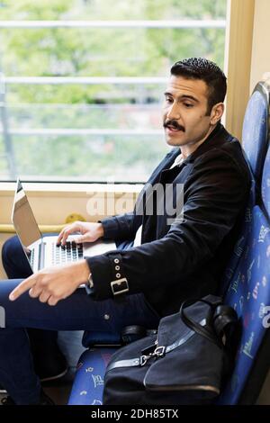 Vista laterale di un giovane uomo che punta mentre si utilizza il computer portatile tram Foto Stock