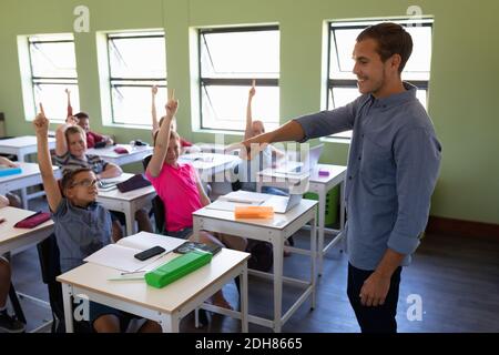 Insegnante di scuola maschile che si trova in una scuola elementare con un gruppo di bambini Foto Stock