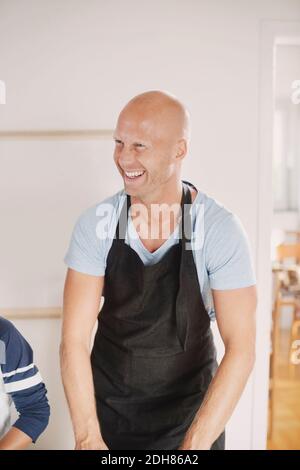 Uomo felice in grembiule che guarda via mentre si trova in cucina Foto Stock