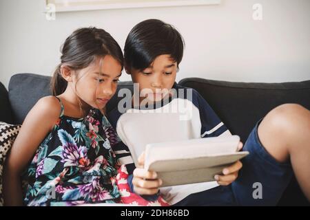 Fratello e Sorella con tavoletta digitale comodamente seduti sul divano di casa Foto Stock